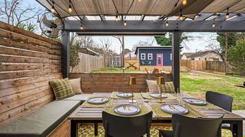 An outdoor dining area with a wooden bench, a table set for four, and a pergola overhead.