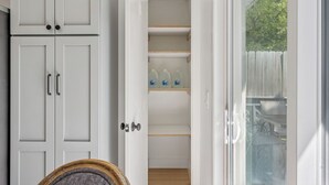 Een kamer met witte kasten, een houten deur en uitzicht op een achtertuin door een glazen deur.
