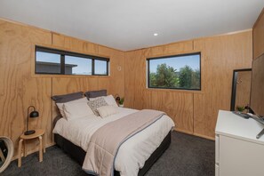 A bedroom with a bed, a desk, and two windows. - Light-filled Sun House - Matarangi Holiday Home (Matarangi)