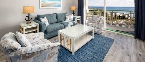 Un salon comprenant un canapé, un fauteuil et une table basse, un balcon avec vue sur l’océan et une décoration sur le thème de la marine.