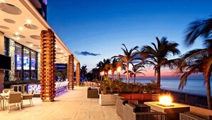 Ein Hotel direkt am Strand mit Außenbestuhlung, Palmen und Blick auf das Meer.