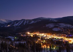 Un pueblo nevado en la noche, con edificios iluminados y un complejo de esquí al fondo.