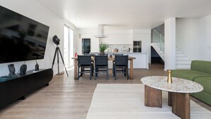 Una sala de estar moderna con un televisor de pantalla plana, un comedor con mesa y sillas, un sofá verde y una escalera que sube a un nivel superior.