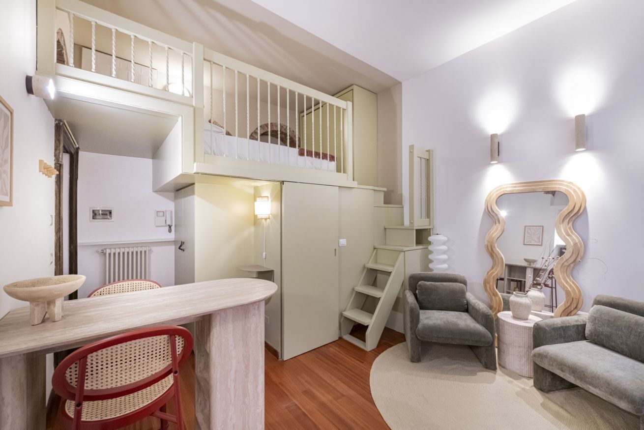 A compact living space with a loft bedroom, a dining area with a round table and chairs, and a seating area with a sofa and armchairs.