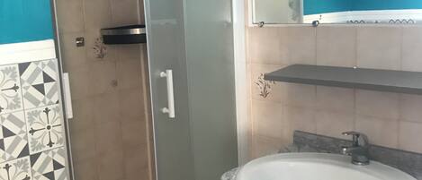 Un baño con cabina de ducha de vidrio, un lavamanos blanco con encimera de mármol y un espejo sobre el lavamanos.