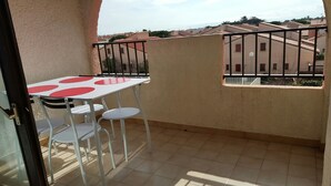 Un balcón con mesa y sillas, vistas a edificios cercanos y suelo de baldosas.
