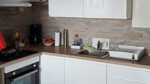Una cocina moderna con armarios blancos, horno empotrado, lavabo y cafetera.