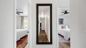 Un pasillo con un espejo que refleja un dormitorio con una cama, un ventilador de techo y un cuadro en la pared.