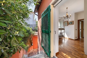 Una habitación con piso de madera, una puerta con contraventanas verdes y una araña.