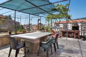 Una terrazza esterna con tavolo e sedie, un barbecue e piante in vaso.