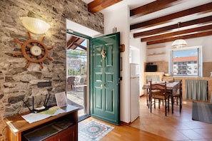 Una habitación con pared de piedra, puerta verde, techo de madera, una mesa de comedor con sillas y vistas al exterior.