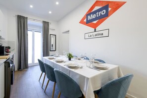 Ein Essbereich mit einem langen Tisch, gedeckt für vier Personen, ein Küchenbereich zur Linken und ein Schild mit der Aufschrift Metro La Latina an der Wand.