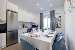 A modern kitchen with a stainless steel refrigerator, white cabinets, and a dining area set for six with blue chairs. - Palacio Real DownTown. 5BR 3BTH. NEW (Madrid)