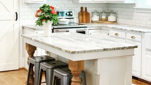 Una cocina con armarios blancos, encimera de mármol y una isla central con taburetes.