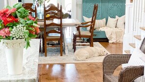 Una sala de estar acogedora con piso de madera, una mesa de comedor con sillas, un sofá y una silla de mimbre.