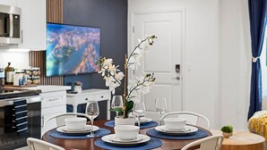 En matplats med ett runt bord för fyra personer, vita tallrikar och klara glas. En stor tv-skärm är monterad på väggen ovanför bordet.