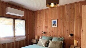 A wooden-paneled bedroom with a bed, bedside lamps, a picture on the wall, and an air conditioning unit.