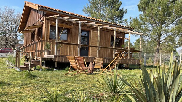 A wooden cabin with a deck, two chairs, and a staircase leading to the upper level.