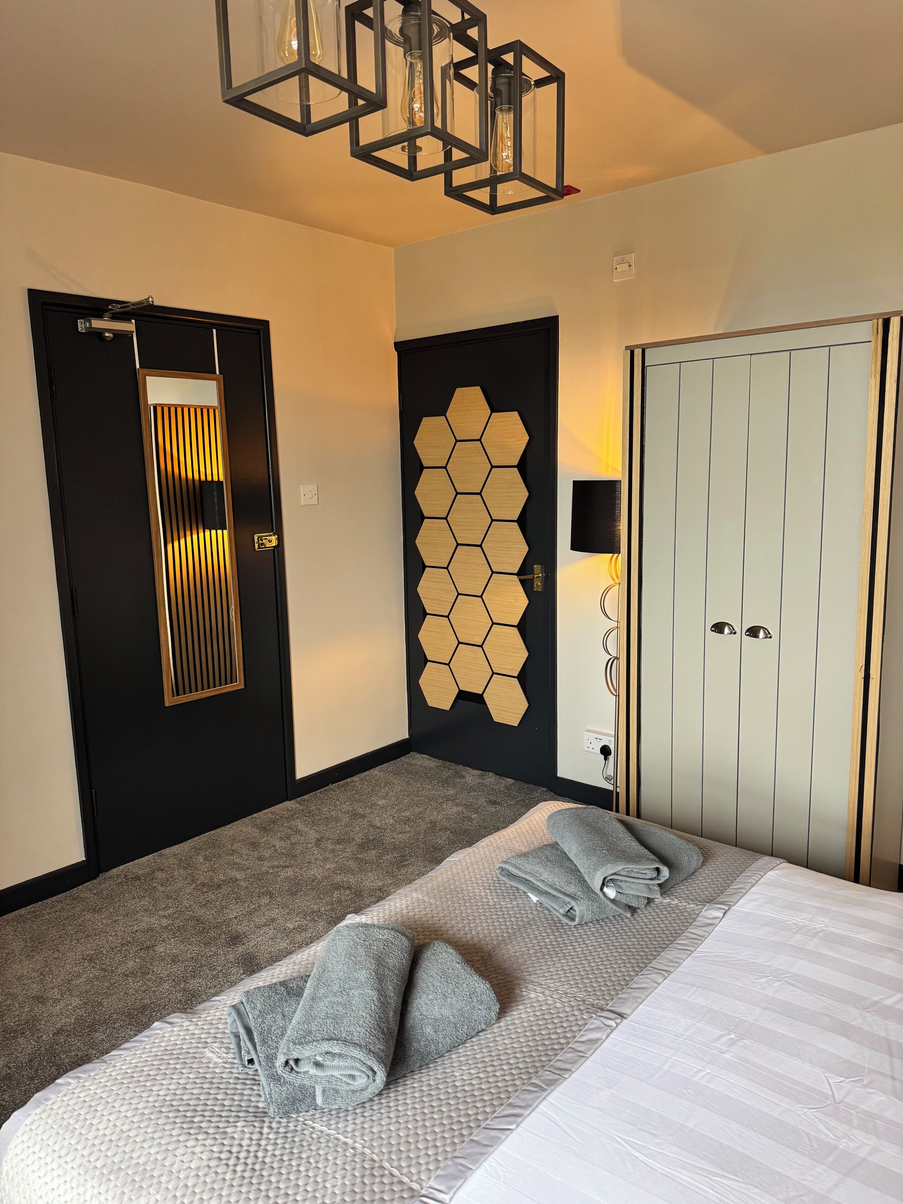 A hotel room with a bed, a wardrobe, a door with a mirror, and a wall with hexagonal panels.