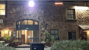 L’extérieur de l’hôtel Craven Hill se distingue par sa façade en pierre, son entrée en arc de cercle bien visible et une enseigne lumineuse placée au-dessus de la porte.