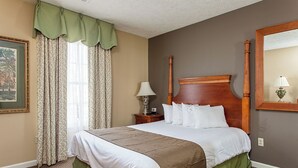 Hotellihuone, jossa on suuri sänky, yöpöytä lampun kanssa, peili ja seinällä oleva kehystetty kuva.