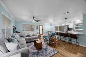 A living room with a gray sofa, patterned armchair, and round coffee table. There is a kitchen area with a bar and stools. - Fish/Relax at Lakefront Retreat Sleeps 10 Pets OK (Conroe)