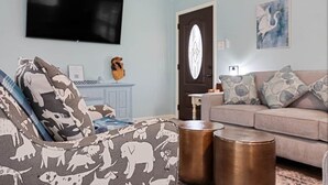 A living room with a sofa, a television mounted on the wall, a door with an oval mirror, and a framed picture on the wall.