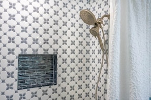 A bathroom with patterned tiles, a showerhead, and a window with a metal grille. - Fish/Relax at Lakefront Retreat Sleeps 10 Pets OK (Conroe)