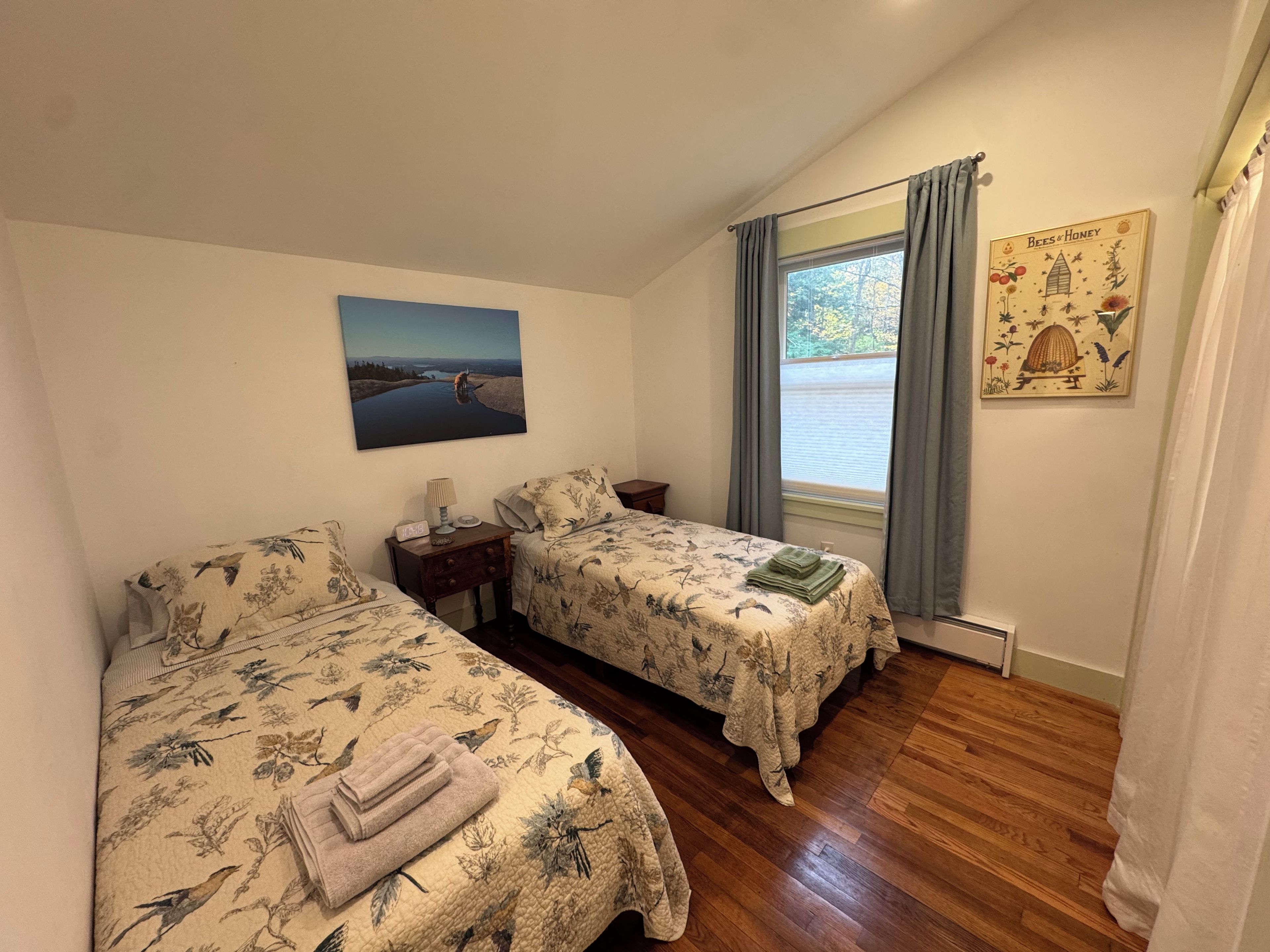 A room with two beds, a painting, a window with curtains, and a wall decoration.