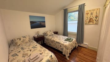A room with two beds, a painting, a window with curtains, and a wall decoration.