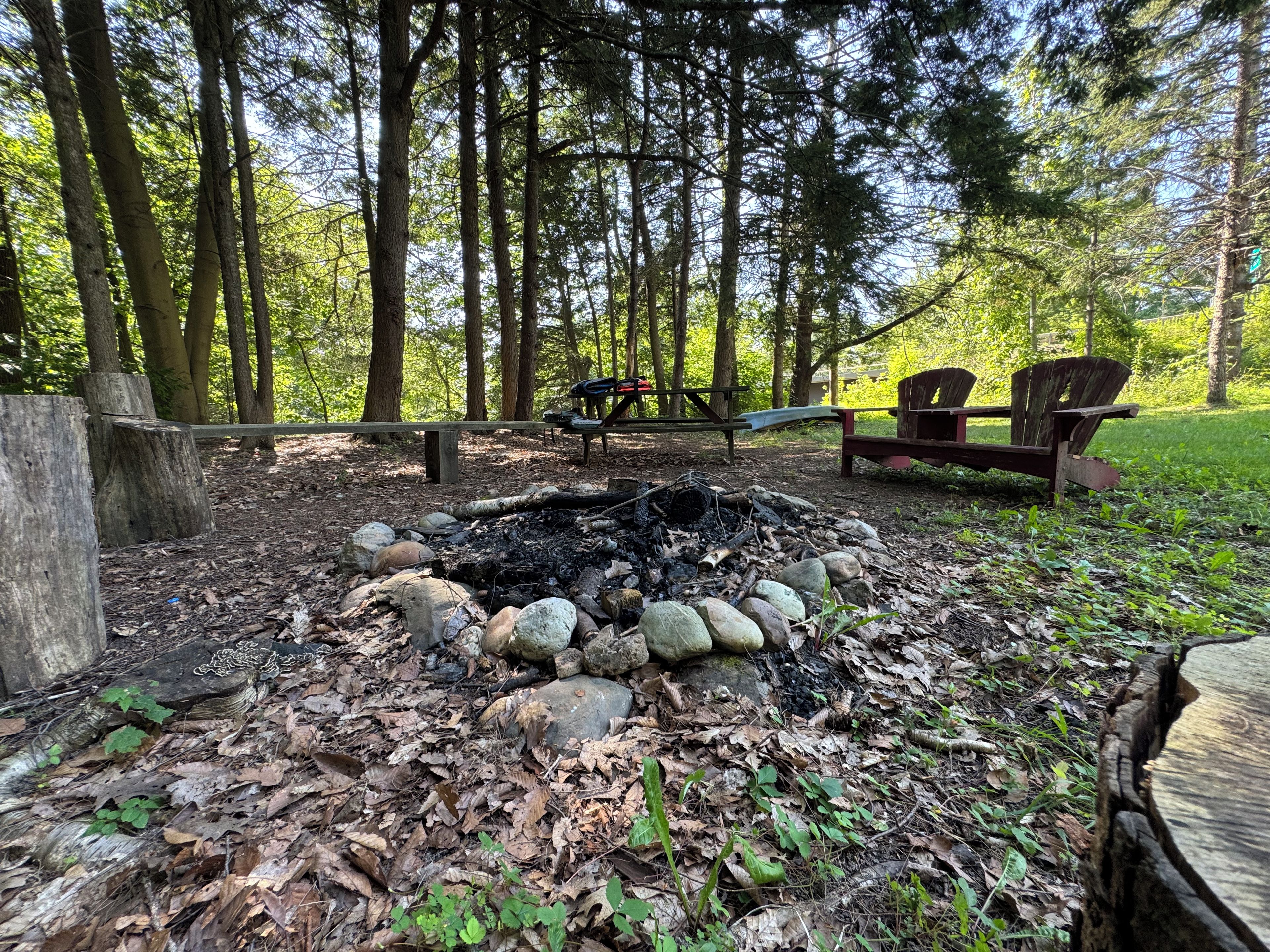 Un campamento con un brasero rodeado de rocas, bancos de madera y una mesa de picnic.