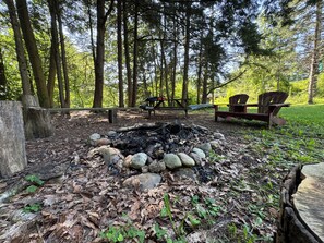 A campsite with a fire pit surrounded by rocks, wooden benches, and a picnic table. - Little River Cottage (Salem)
