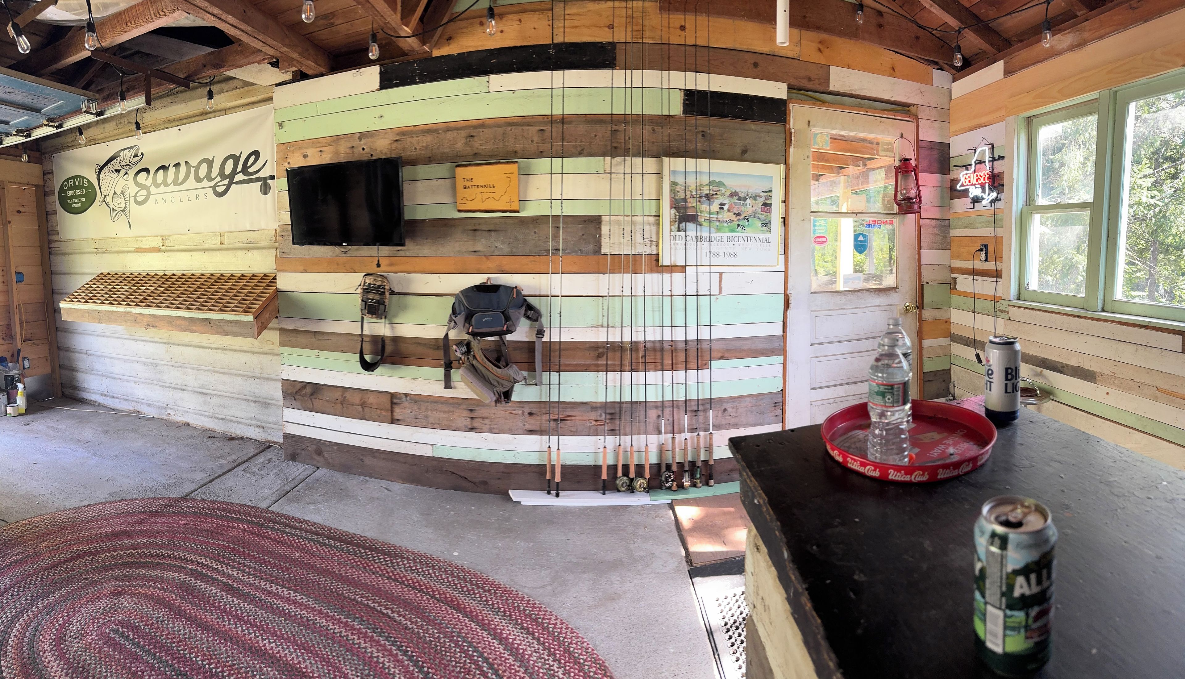 L’intérieur d’un chalet rustique présente un mur en bois sur lequel est affiché un logo représentant un poisson, ainsi que le nom « Savage Anglers ».