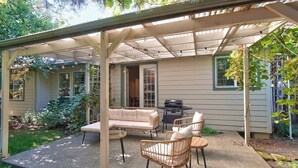 A covered patio with a sofa, chairs, and a grill. - Parkview Place - Wine Country Home with Jetted Tub (McMinnville)