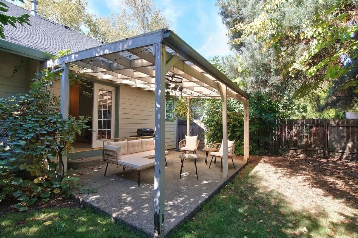 Un patio cubierto con mobiliario exterior, una parrilla y una valla de madera al fondo.