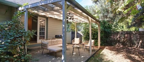 Un patio cubierto con mobiliario exterior, una parrilla y una valla de madera al fondo.