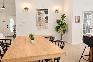 Un coin repas avec une table en bois, des chaises noires, une plante en pot et une tapisserie au mur.
