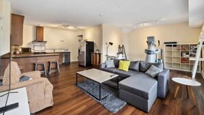 Una sala de estar moderna con un sofá, una mesa de centro y una pequeña mesa redonda. Cuenta con una zona de cocina con un refrigerador y un microondas.