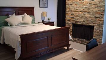 A bedroom with a wooden bed, a stone wall, a fireplace, and a ceiling fan.