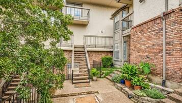 A residential building with a staircase leading to a balcony, surrounded by greenery and potted plants.