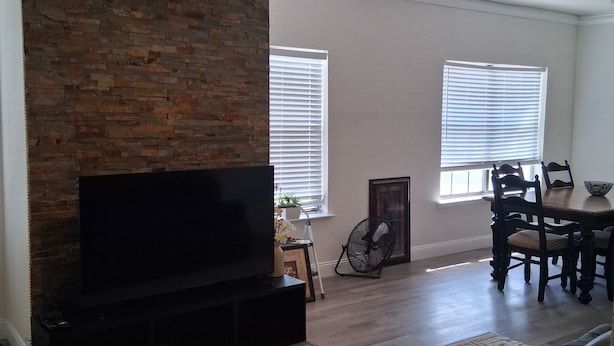 A living room with a brick wall, a ceiling fan, a flat-screen TV, a dining table with chairs, and a fireplace. - Modern 2 bedroom with 2 fire places and a 9 mile walking/biking trail (Dallas)