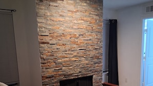 A bedroom with a stone accent wall, a bed with a quilted cover, and a window with blinds. - Modern 2 bedroom with 2 fire places and a 9 mile walking/biking trail (Dallas)