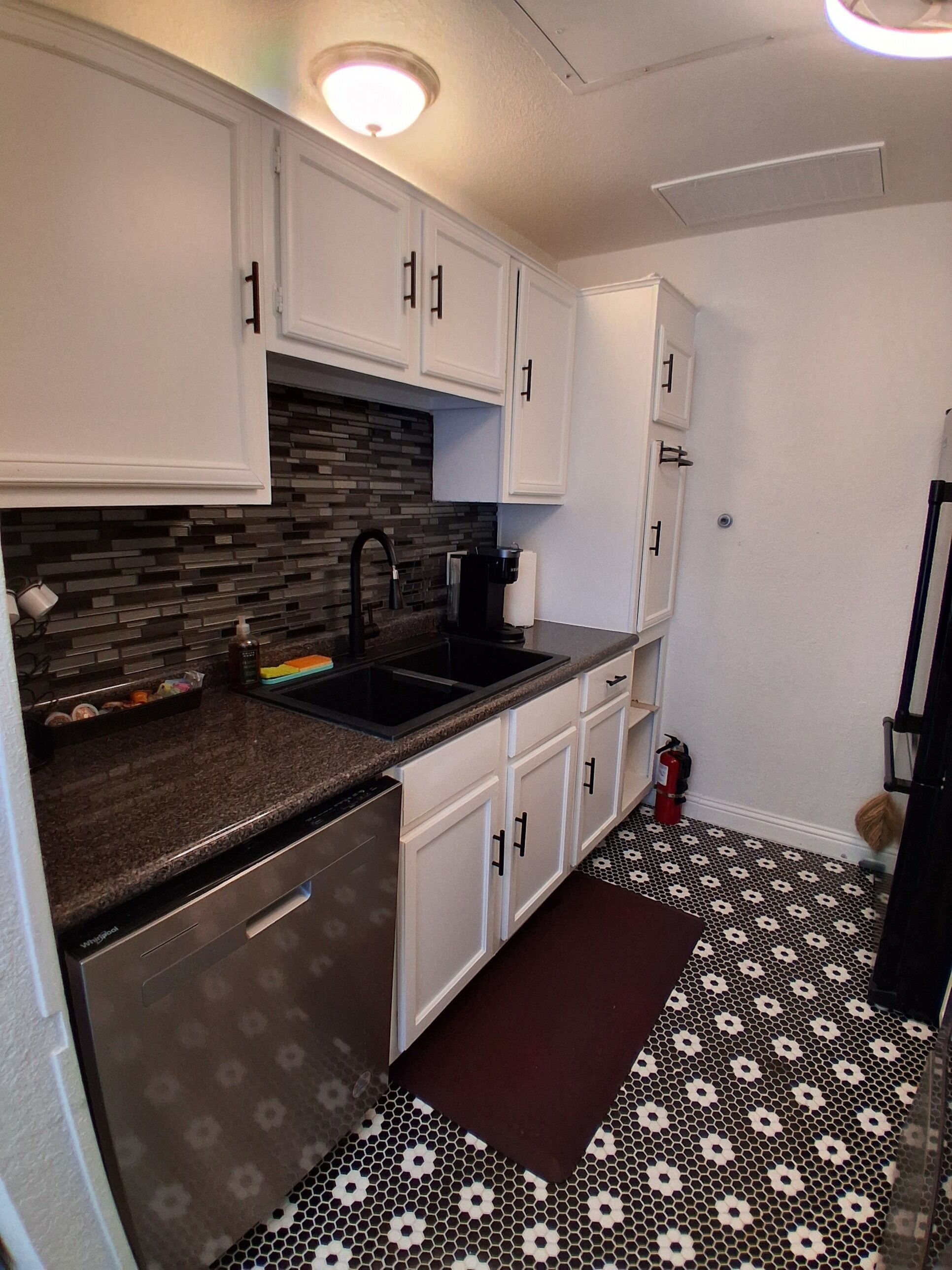 A compact kitchen with white cabinets, a granite countertop, a black faucet, and a coffee maker.