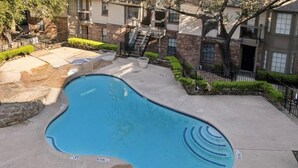A swimming pool with a curved edge, surrounded by a paved deck and a stone wall. - Modern 2 bedroom with 2 fire places and a 9 mile walking/biking trail (Dallas)
