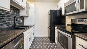 A compact kitchen with white cabinets, a black refrigerator, a microwave, and an oven. - Modern 2 bedroom with 2 fire places and a 9 mile walking/biking trail (Dallas)