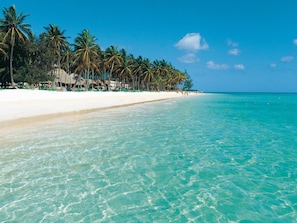 A beach with clear turquoise water, white sand, and palm trees. - Luxurious 4-bedroom Villa With Private Pool in Punta Cana (Punta Cana)