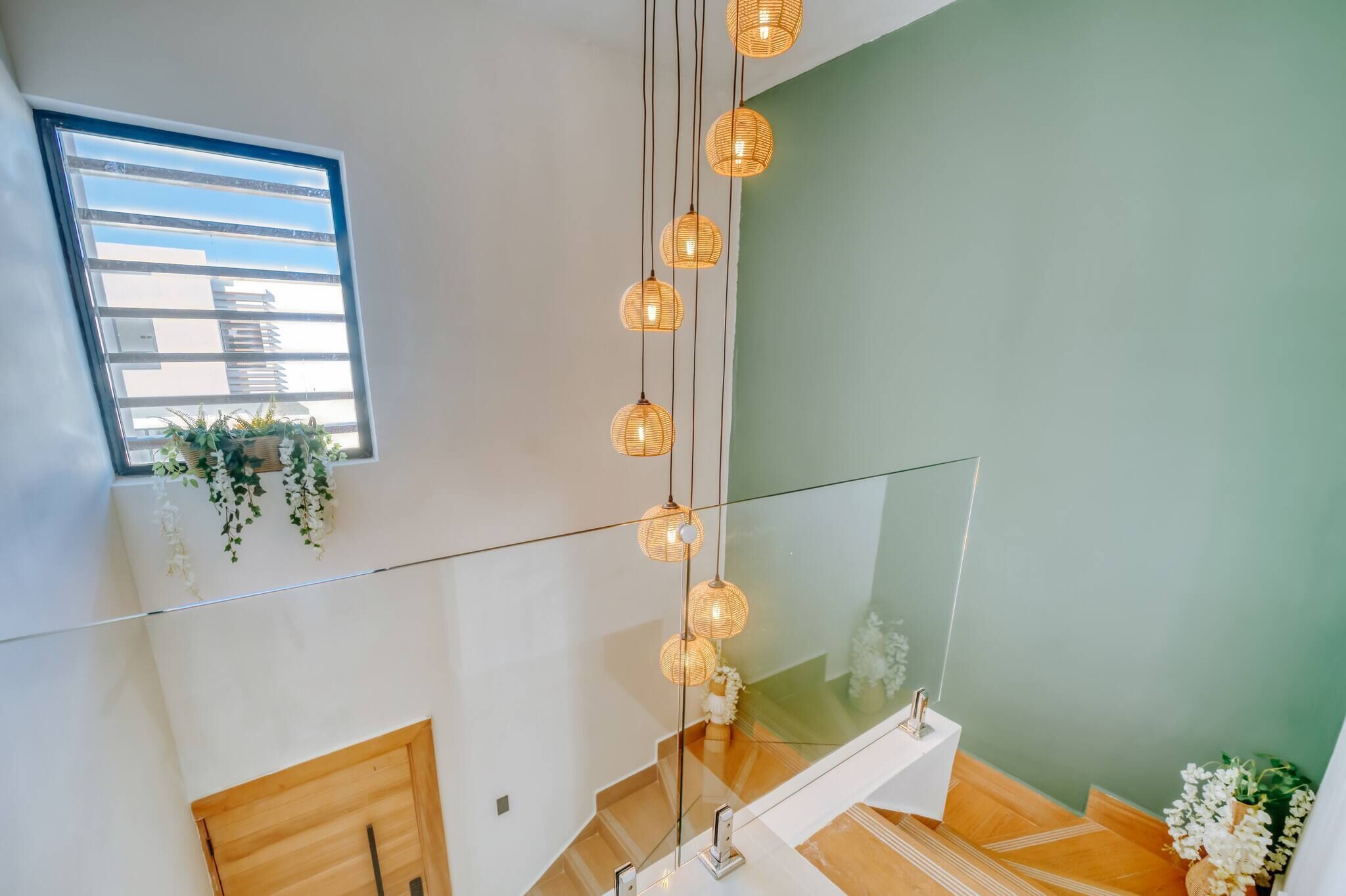 A modern interior with a glass railing, a white sink, and hanging wicker lights.