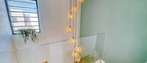 A modern interior with a glass railing, a white sink, and hanging wicker lights.