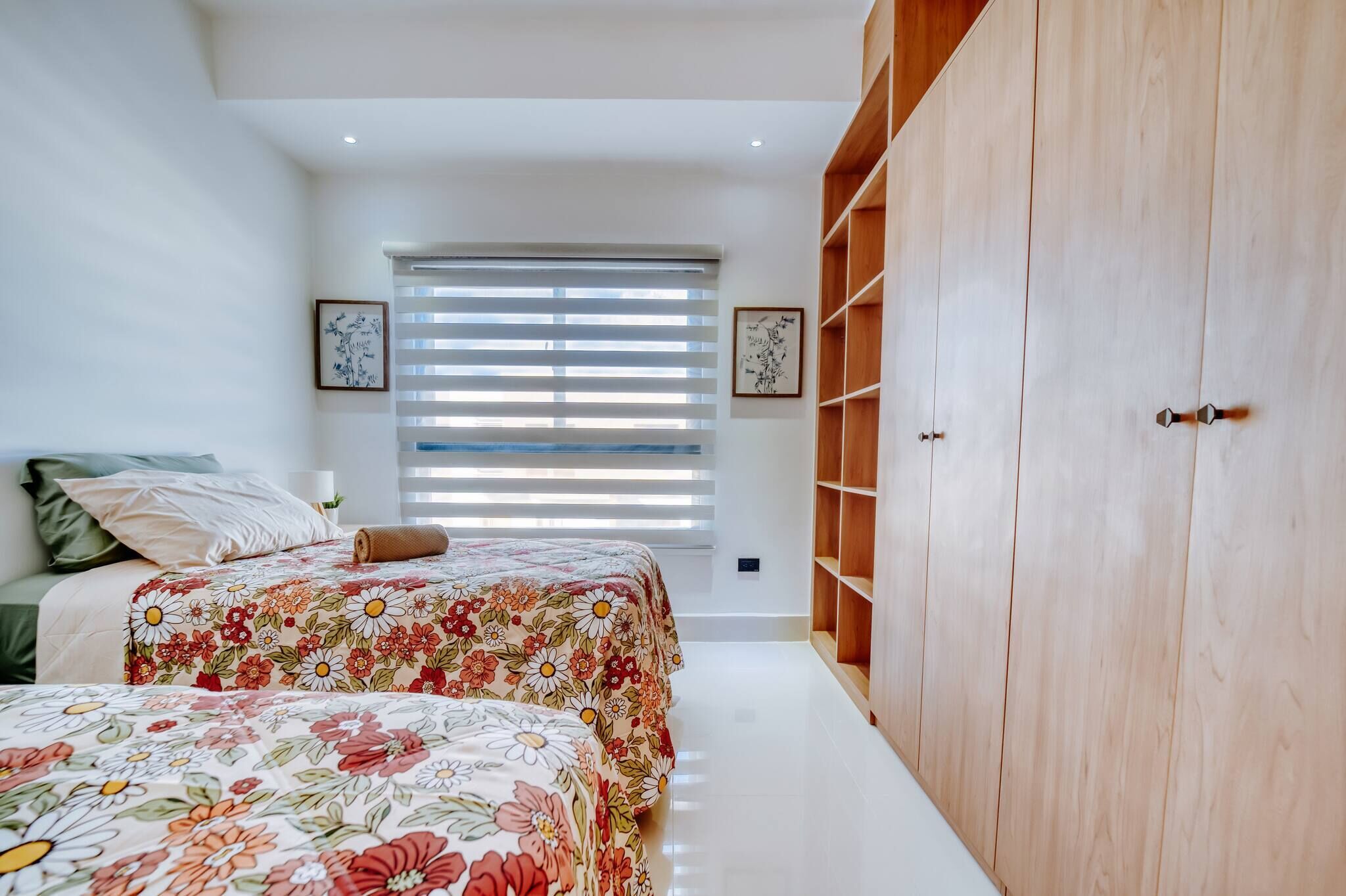 A bedroom with two beds, a large wardrobe, and a window with blinds.
