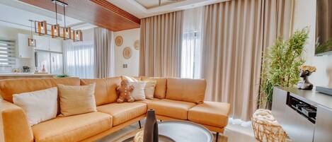 A modern living room with a sectional sofa, a round coffee table, and a kitchen area with a dishwasher.